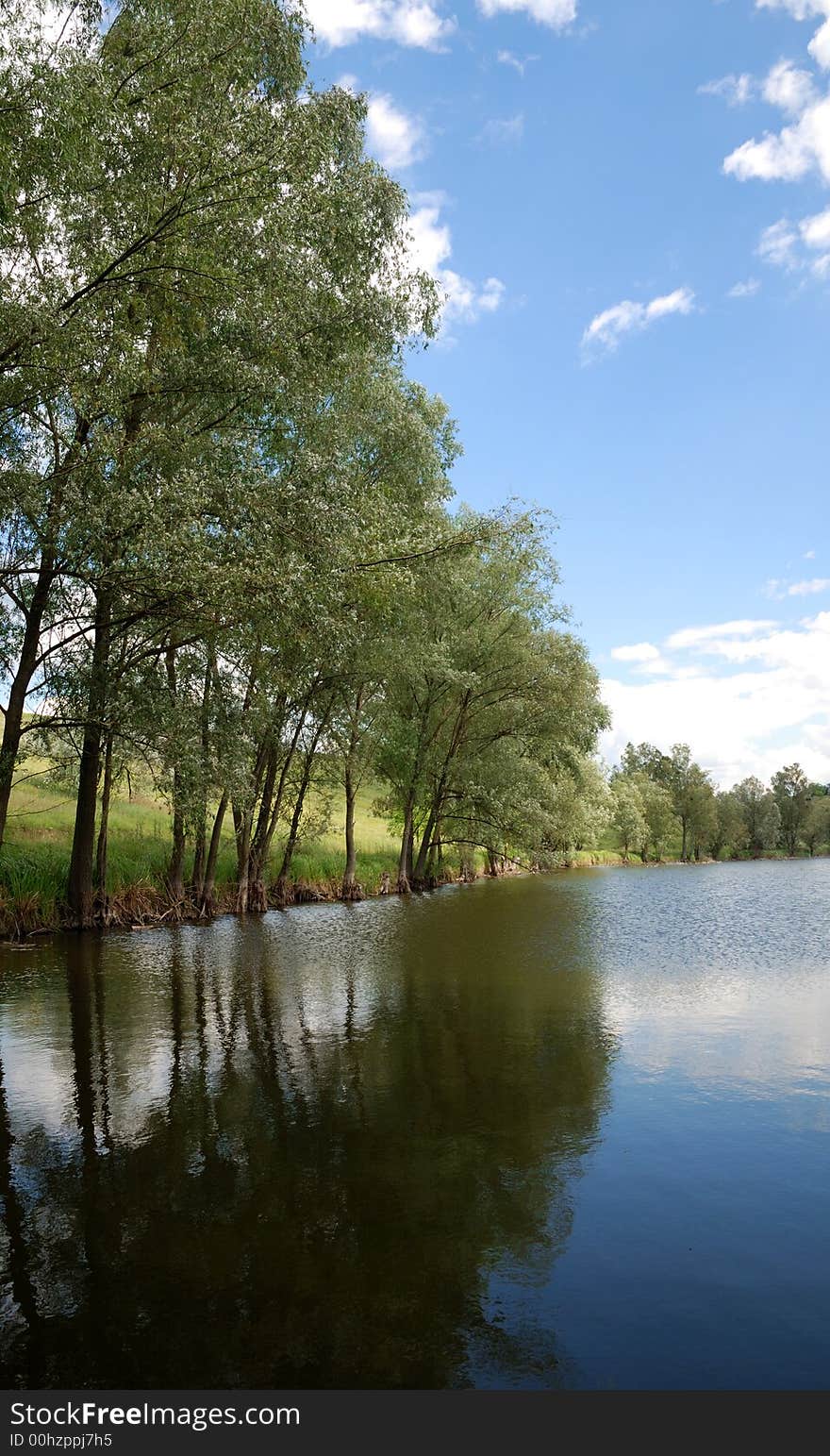 Beautiful landscape. Green hills and lake with trees on bank.