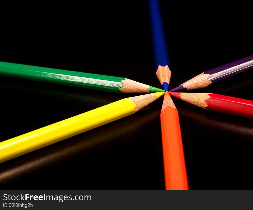 Colored pencils, blue, purple, red, orange, yellow, and green on a black background. The pencils are arranged so that the primary colors are outside each of the secondary colors they create.