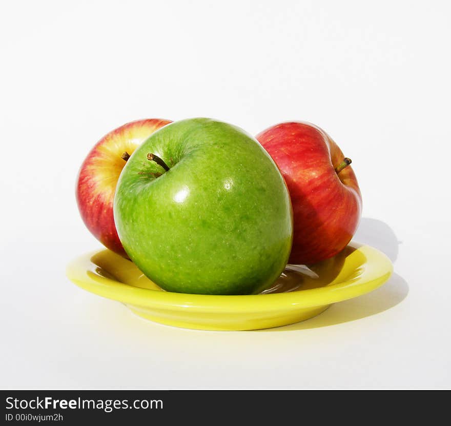 One green and two red apples lay on a yellow plate. One green and two red apples lay on a yellow plate.