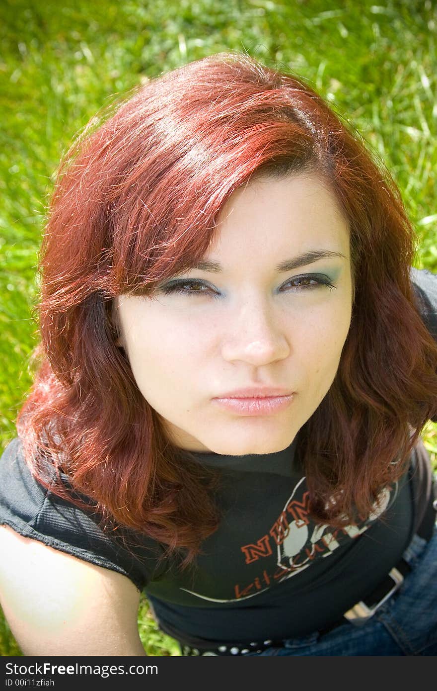 A pretty young woman looks into the camera while sitting on the grass. A pretty young woman looks into the camera while sitting on the grass.