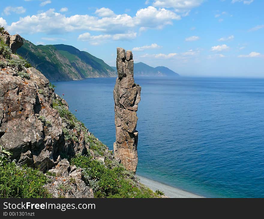 On foreground the single vertical rock with name Hare. On background turquoise sea, cliffs and sky with white clouds. Russian Far Easr, Primorye, Japanese sea, Tasovaya Bay. On foreground the single vertical rock with name Hare. On background turquoise sea, cliffs and sky with white clouds. Russian Far Easr, Primorye, Japanese sea, Tasovaya Bay.