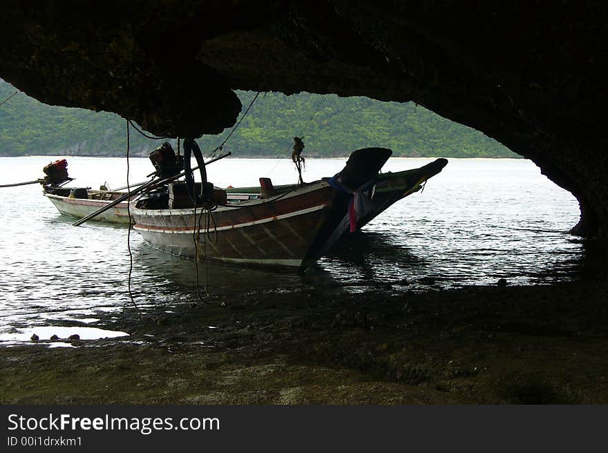 Two thai long boats moored on an island next to a large rock. Two thai long boats moored on an island next to a large rock