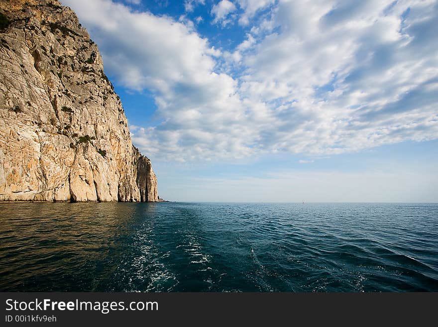 After-tossing of the ship floating across Black sea. The steep rock and the cloudy sky is seen. After-tossing of the ship floating across Black sea. The steep rock and the cloudy sky is seen