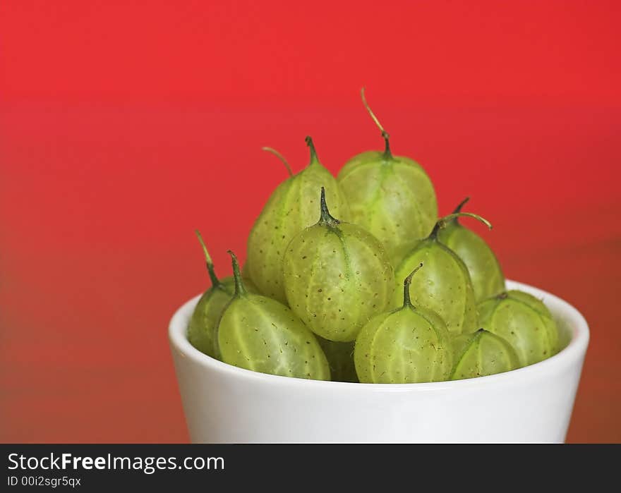 A white bowl filled with fresh gooseberries. On a red background. A white bowl filled with fresh gooseberries. On a red background.