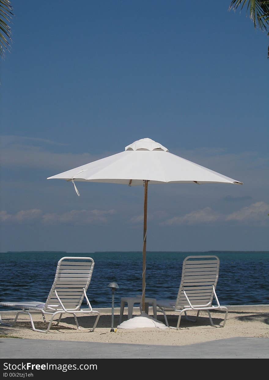 Two beach loungers and an umbrella sit by the water. Two beach loungers and an umbrella sit by the water