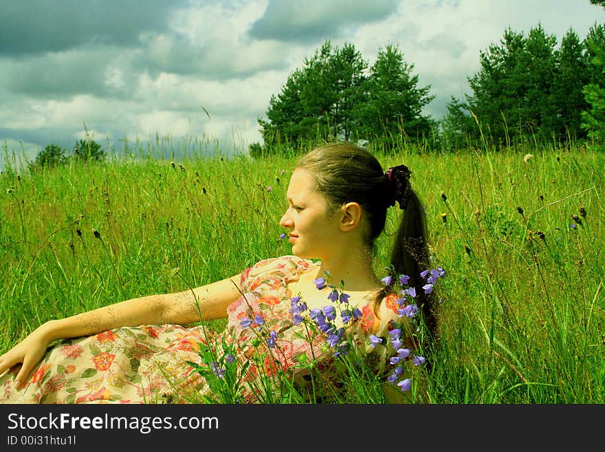 The young girl lays in the years warm afternoon in a green grass. Beside flowers grow in a floor. It has a rest behind city and is happy. The young girl lays in the years warm afternoon in a green grass. Beside flowers grow in a floor. It has a rest behind city and is happy.