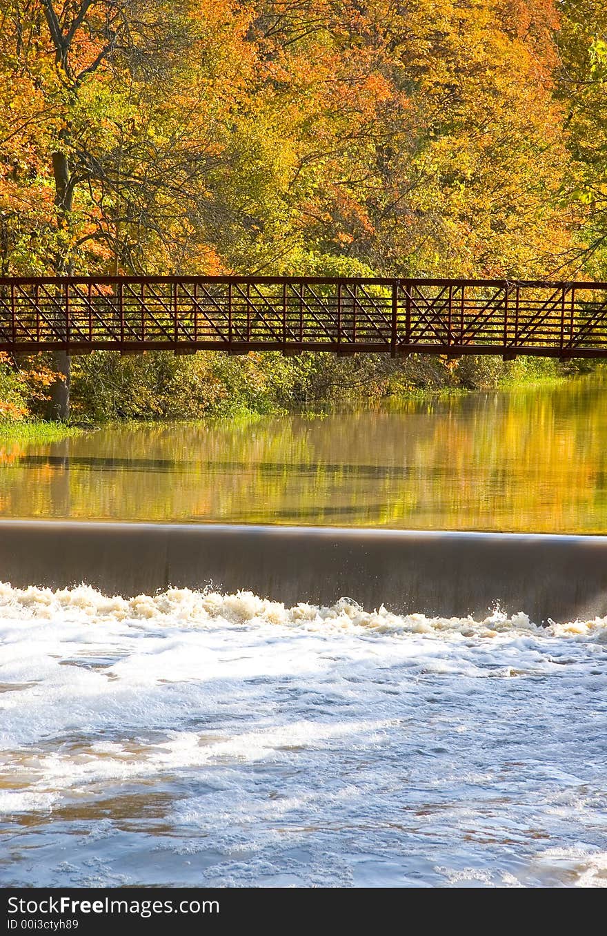 A bridge over calm flowing water, with colorful trees in the background. A bridge over calm flowing water, with colorful trees in the background.