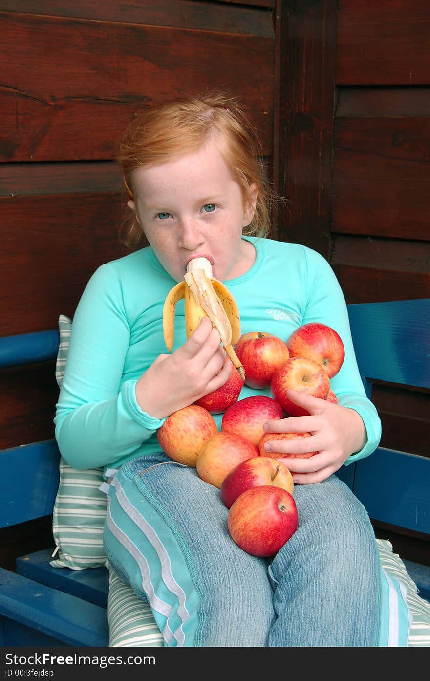 Girl eating banana and holding apples