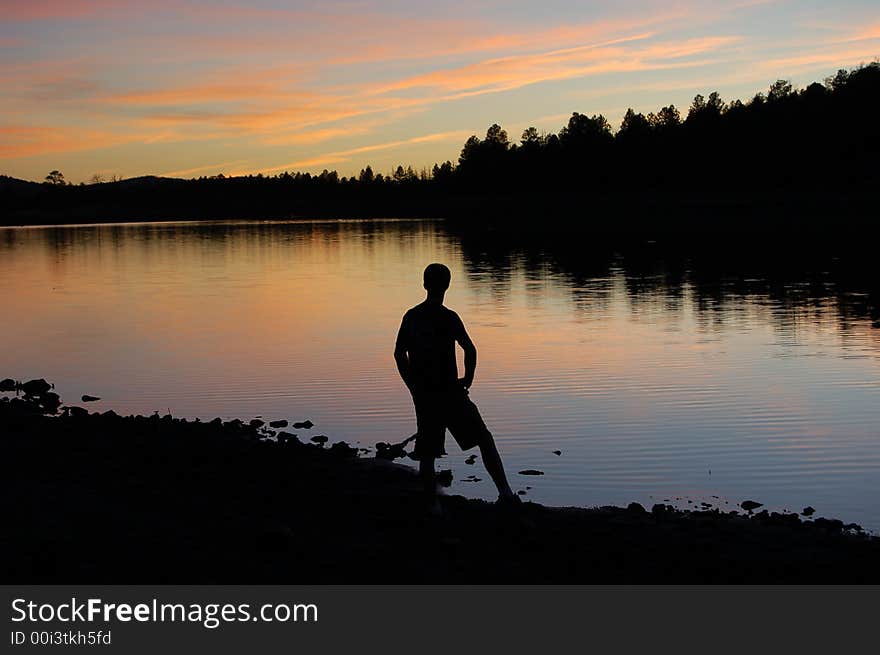 A man watching ths sun go down over the water. A man watching ths sun go down over the water