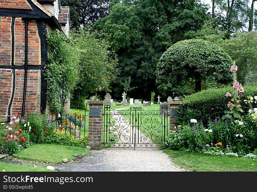 Wrought Iron Entrance Gate to an English Village Churchyard with flowers and Timber Framed Cottage. Wrought Iron Entrance Gate to an English Village Churchyard with flowers and Timber Framed Cottage