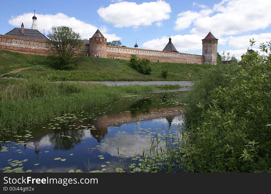 Long red wall and towers of old Russian fort-monastery by the river. Summer. Long red wall and towers of old Russian fort-monastery by the river. Summer