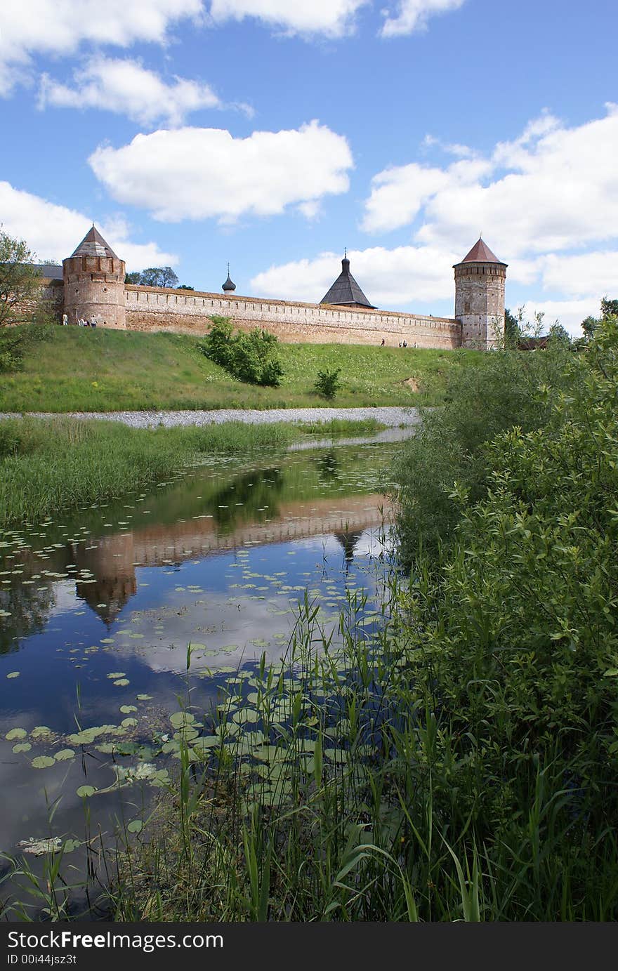 Long red wall and towers of old Russian fort-monastery by the river. Summer. Long red wall and towers of old Russian fort-monastery by the river. Summer