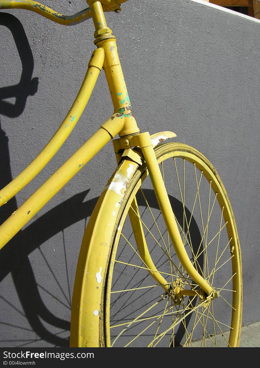 The front wheel of an old yellow bike leaning on a grey wall. The front wheel of an old yellow bike leaning on a grey wall