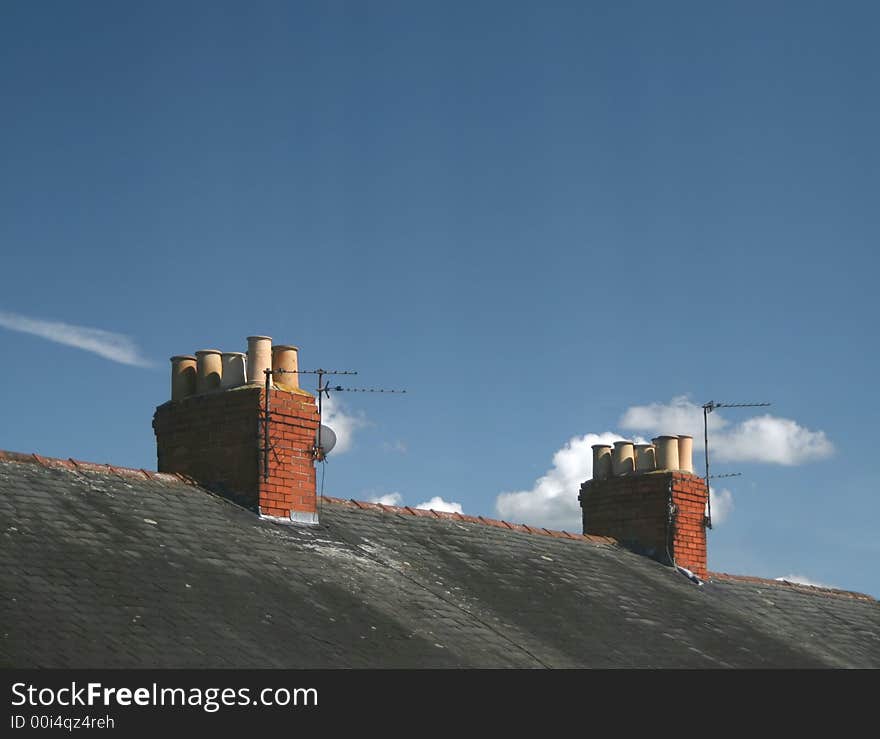 Red brick chimneys on terraced house roofs with blue sky and white clouds. Red brick chimneys on terraced house roofs with blue sky and white clouds