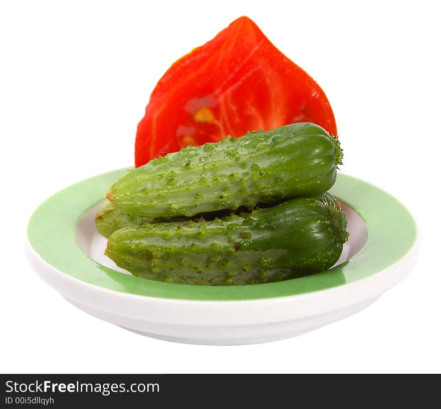 Three little cucumbers with the half of tomato on a dish. Three little cucumbers with the half of tomato on a dish