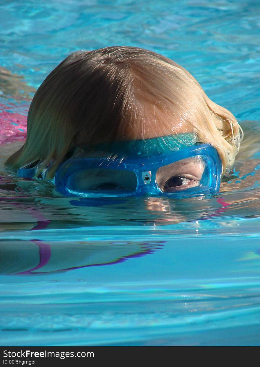 Young girl wearing goggles, with her face partially submerged in a swimming pool. Young girl wearing goggles, with her face partially submerged in a swimming pool.