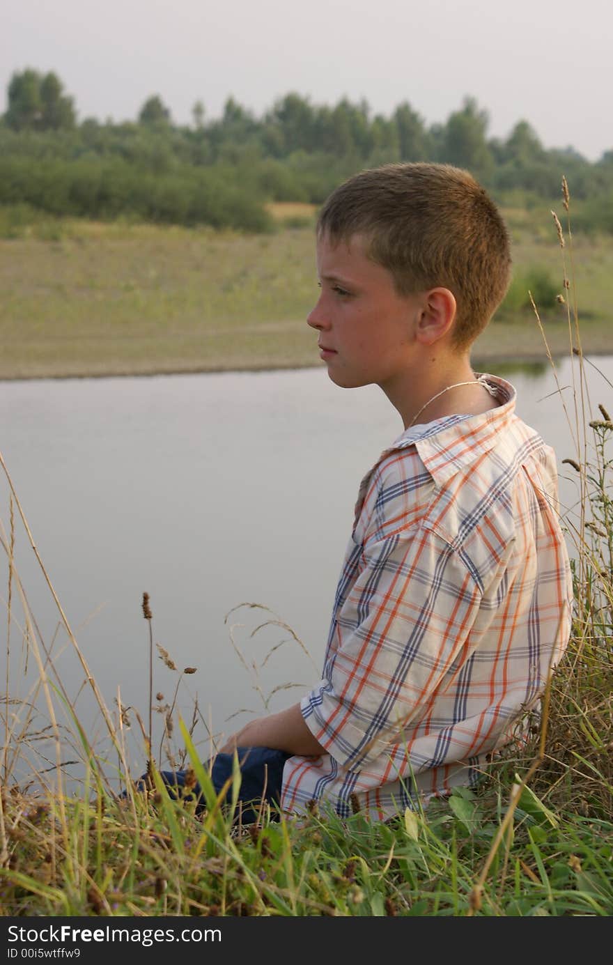 The boy sits on coast of the river. The boy sits on coast of the river