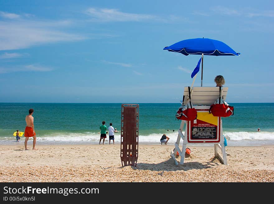 Two young men beach lifeguards watch people swimming in the blue ocean with waves crashing on a sandy beach. Room for text. Two young men beach lifeguards watch people swimming in the blue ocean with waves crashing on a sandy beach. Room for text.