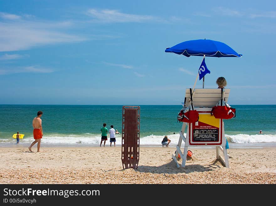 Two young men beach lifeguards watch people swimming in the blue ocean with waves crashing on a sandy beach. Room for text. Two young men beach lifeguards watch people swimming in the blue ocean with waves crashing on a sandy beach. Room for text.