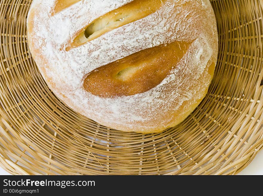 A round loaf of white bread on a woven plate (closeup)