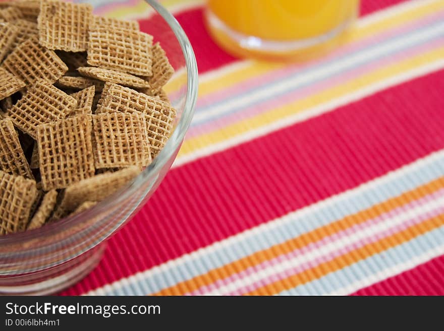 Bowl of cereal and glass of orange juice on a stripy place-mat. Focus on cereal. Bowl of cereal and glass of orange juice on a stripy place-mat. Focus on cereal.