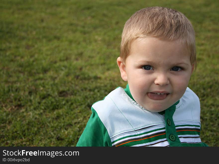 Toddler sitting on the grass, sticking his tongue out. Toddler sitting on the grass, sticking his tongue out