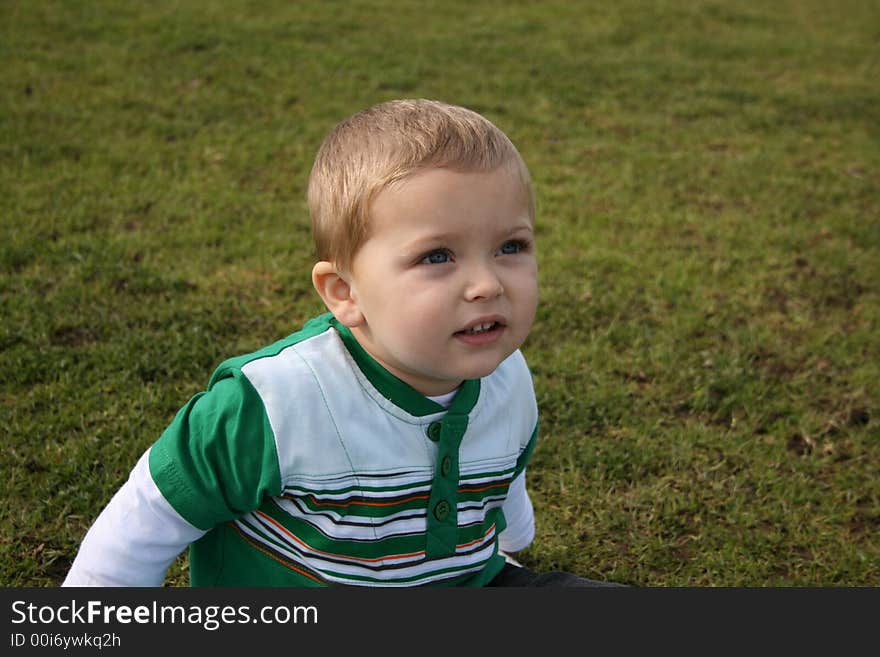 Young boy looking up into the distance, sitting on the grass