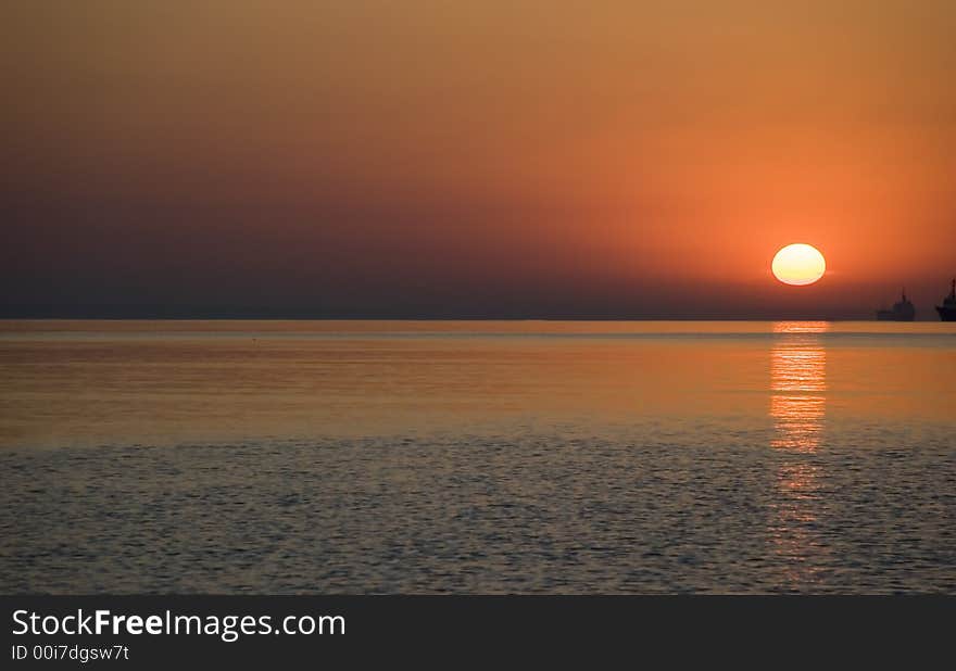 Red sunrise above ocean. With the military ships on a background