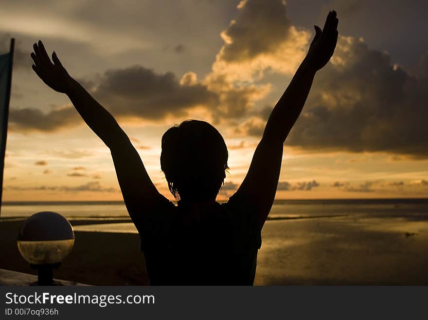 A silhouette of a girls with arms raised during sunset. A silhouette of a girls with arms raised during sunset