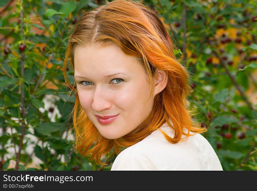 The young attractive girl with brightly painted hair with a happy smile. A portrait on a background of a ripe cherry. Shallow DOF.