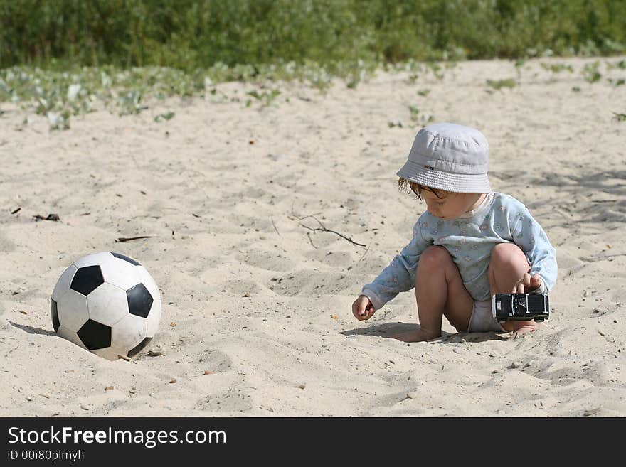 The boy plays on sand with the toy automobile near to a football. The boy plays on sand with the toy automobile near to a football