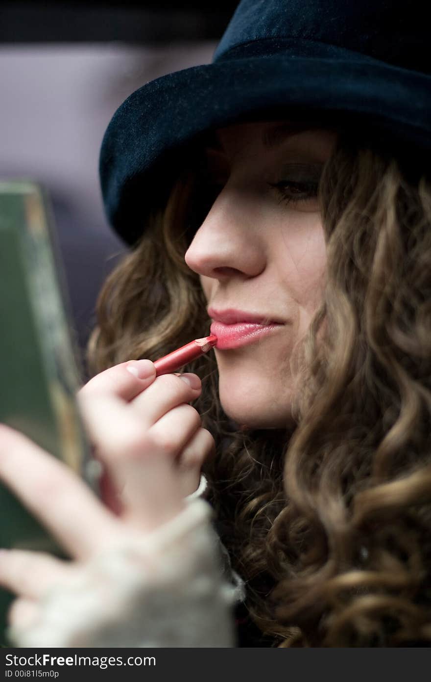 Young model in hat retouching the lips with red pencil