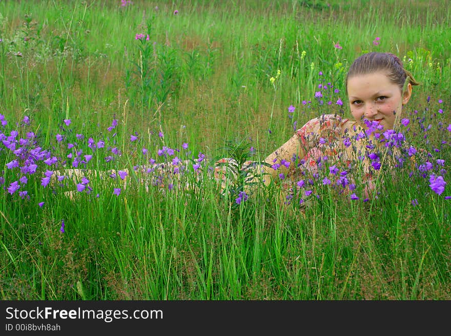 The young girl lays in the years warm afternoon in a green grass. Beside flowers grow in a floor. It has a rest behind city and is happy. The young girl lays in the years warm afternoon in a green grass. Beside flowers grow in a floor. It has a rest behind city and is happy