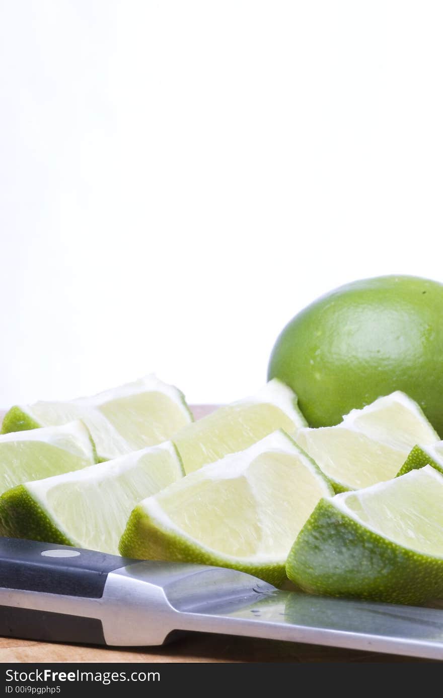 A selection of freshly cut limes with knife in foreground and whole lime in background. A selection of freshly cut limes with knife in foreground and whole lime in background