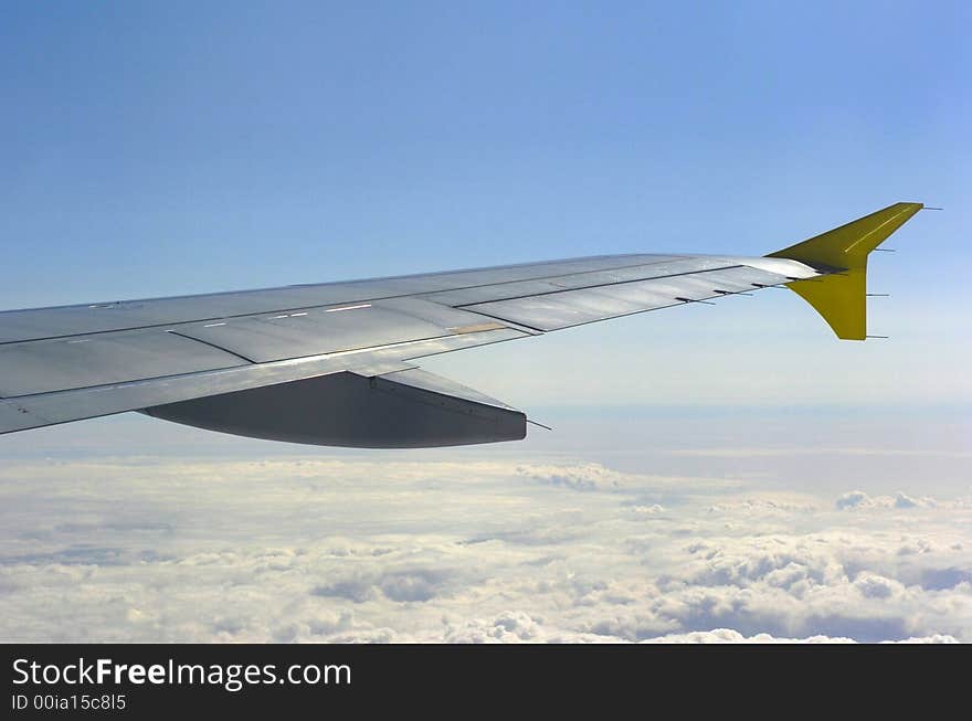 Aircraft winglet in the sun over the clouds up in blue sky