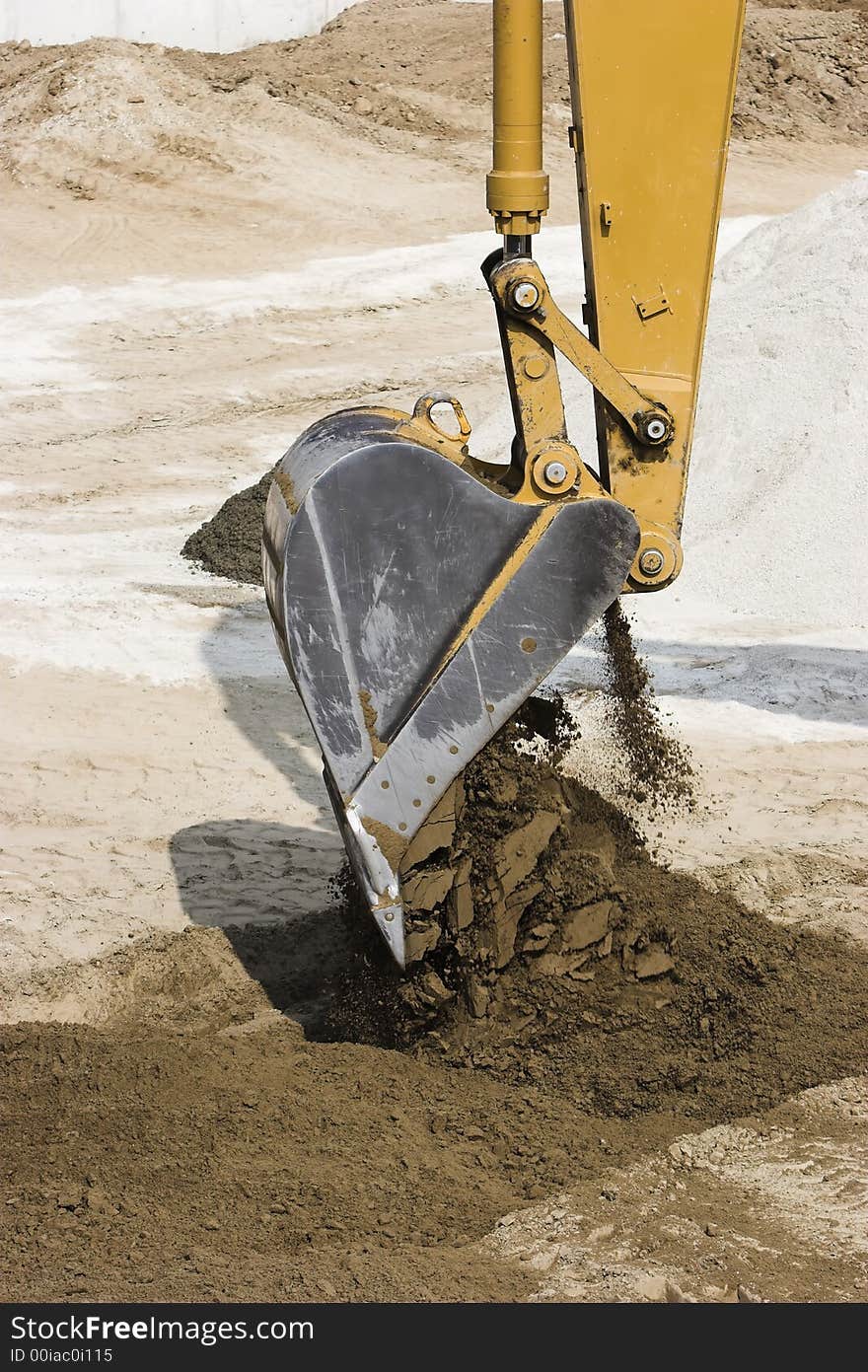 Excavator dumping its load of dirt from its bucket. Vertical format.