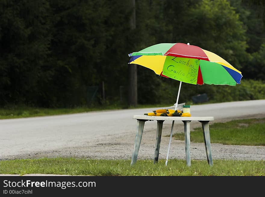 Vegetable table on the side of the road with a very colorful umbrella. Vegetable table on the side of the road with a very colorful umbrella.