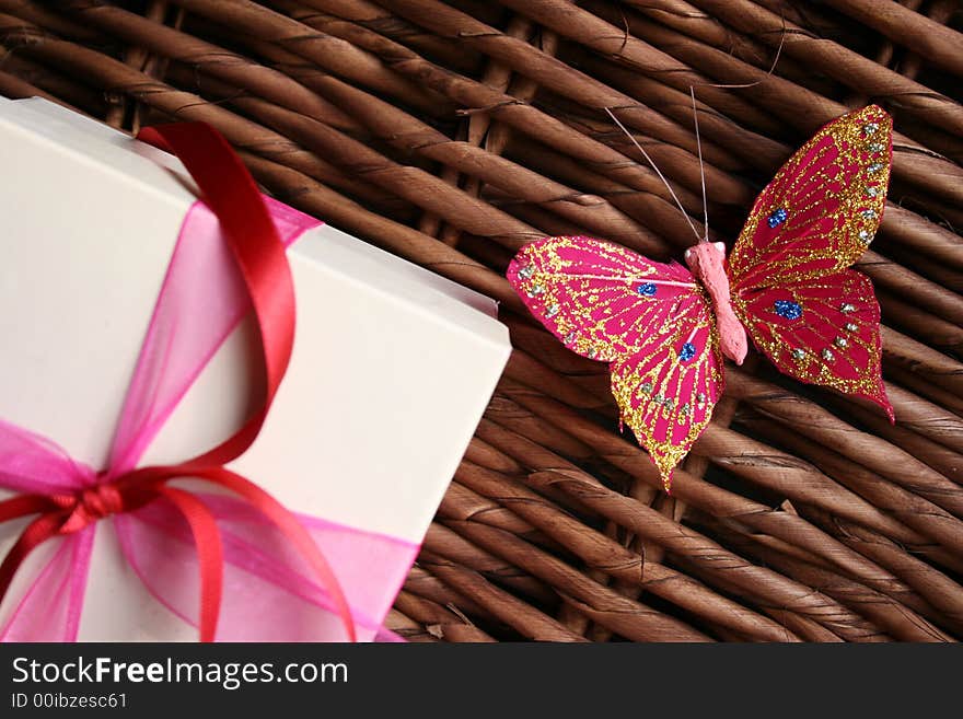 Gift box decorated with ribbons and a butterfly next to it on a woven wood surface. Gift box decorated with ribbons and a butterfly next to it on a woven wood surface