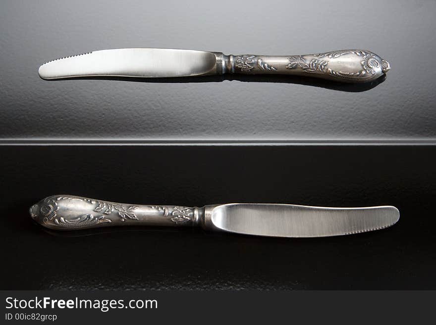 Two table knifes at black steel background.