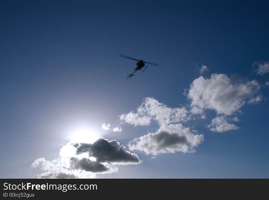 A silhouette of a helicopter with the sun hidden behind scattered clouds and a nice blue sky. A silhouette of a helicopter with the sun hidden behind scattered clouds and a nice blue sky.