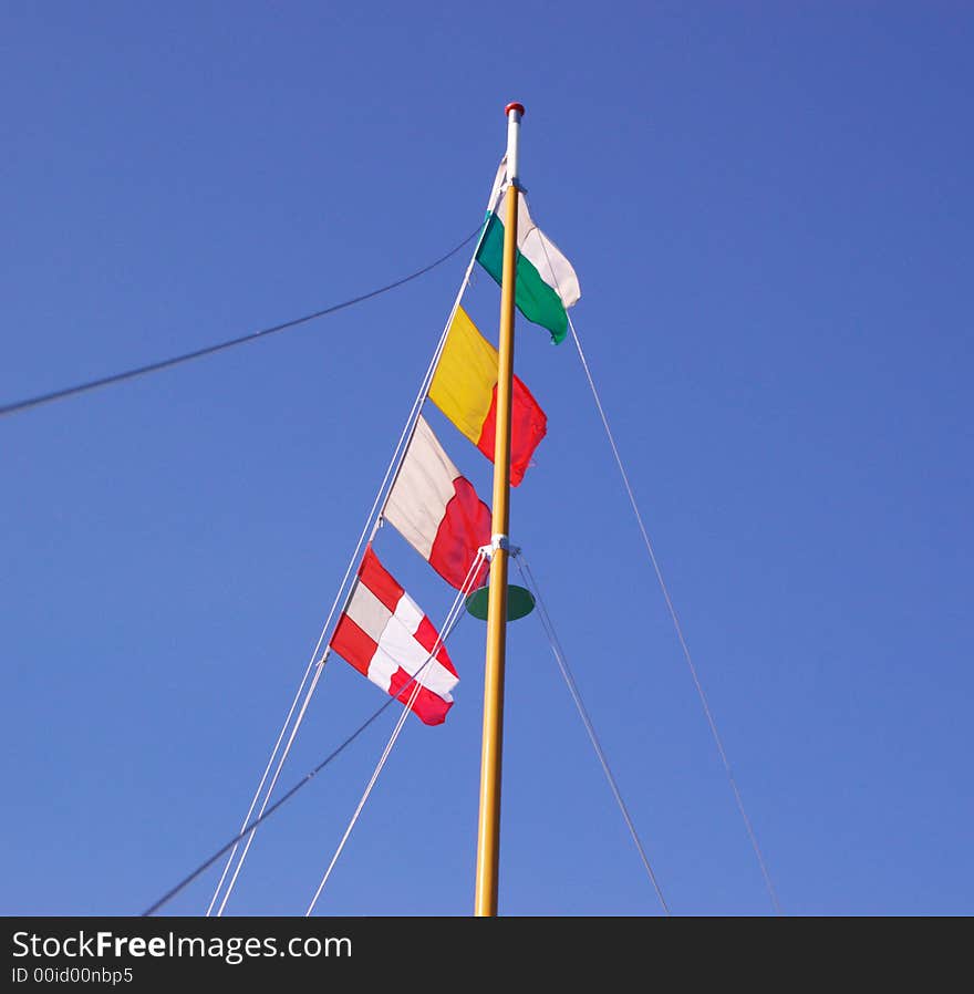 Four marine signal flags on wooden mast in blue sky. Four marine signal flags on wooden mast in blue sky