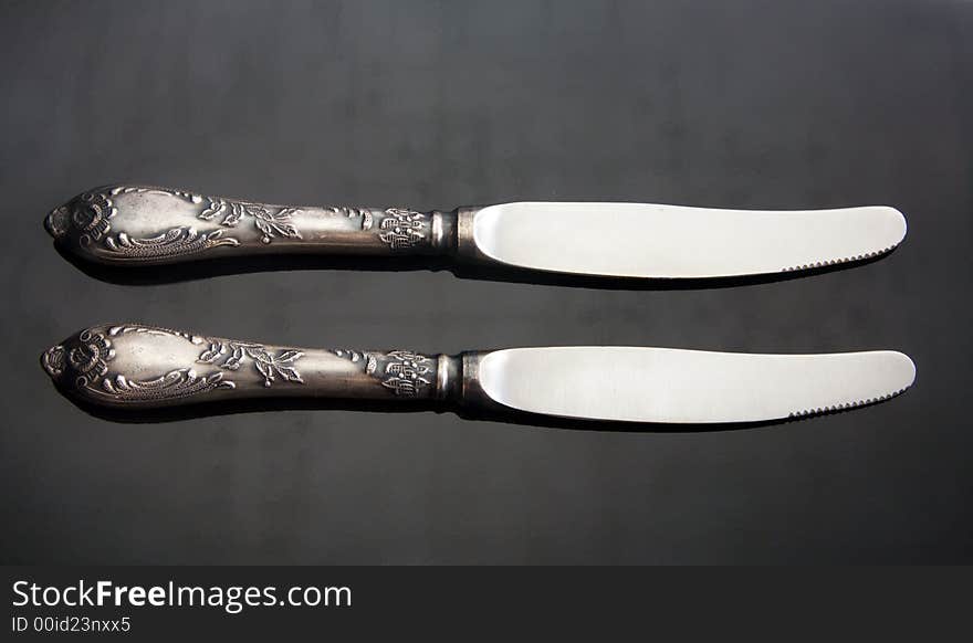 Two table knifes at black steel background.