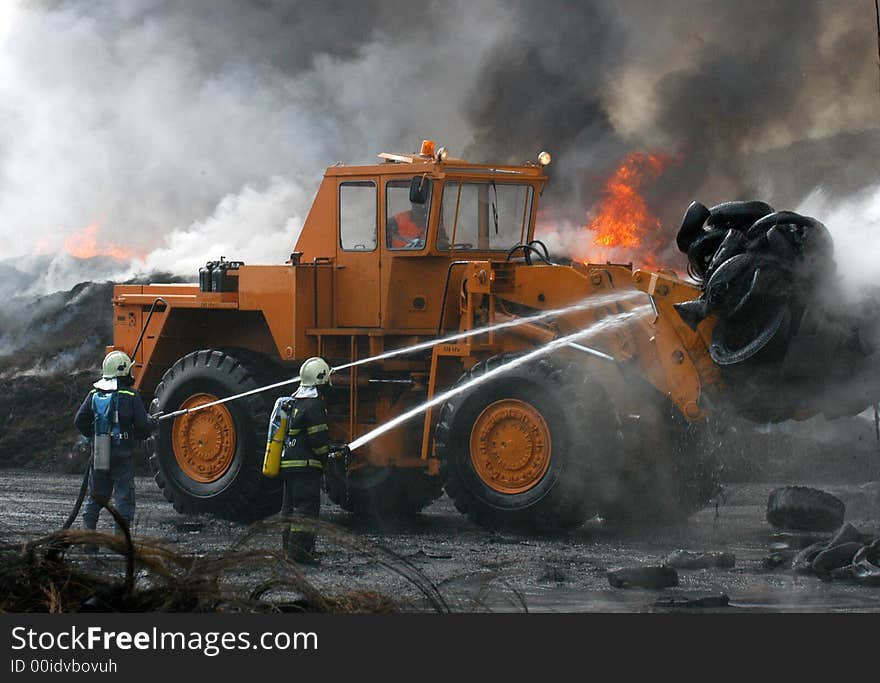 Two Firemen and a digger fighting the fire of tires