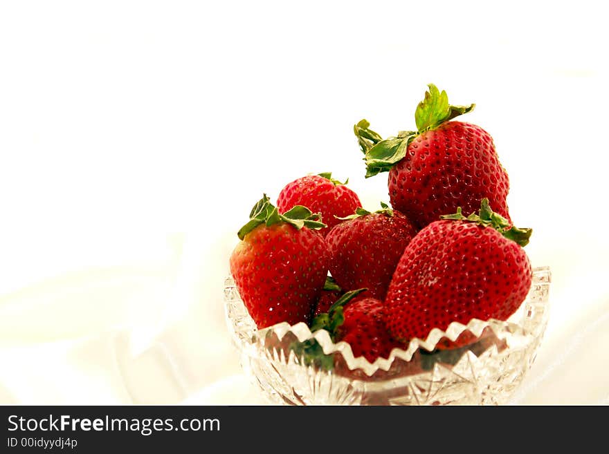 Scrumptuous red strawberries in a crystal bowl against a white satin background. Scrumptuous red strawberries in a crystal bowl against a white satin background