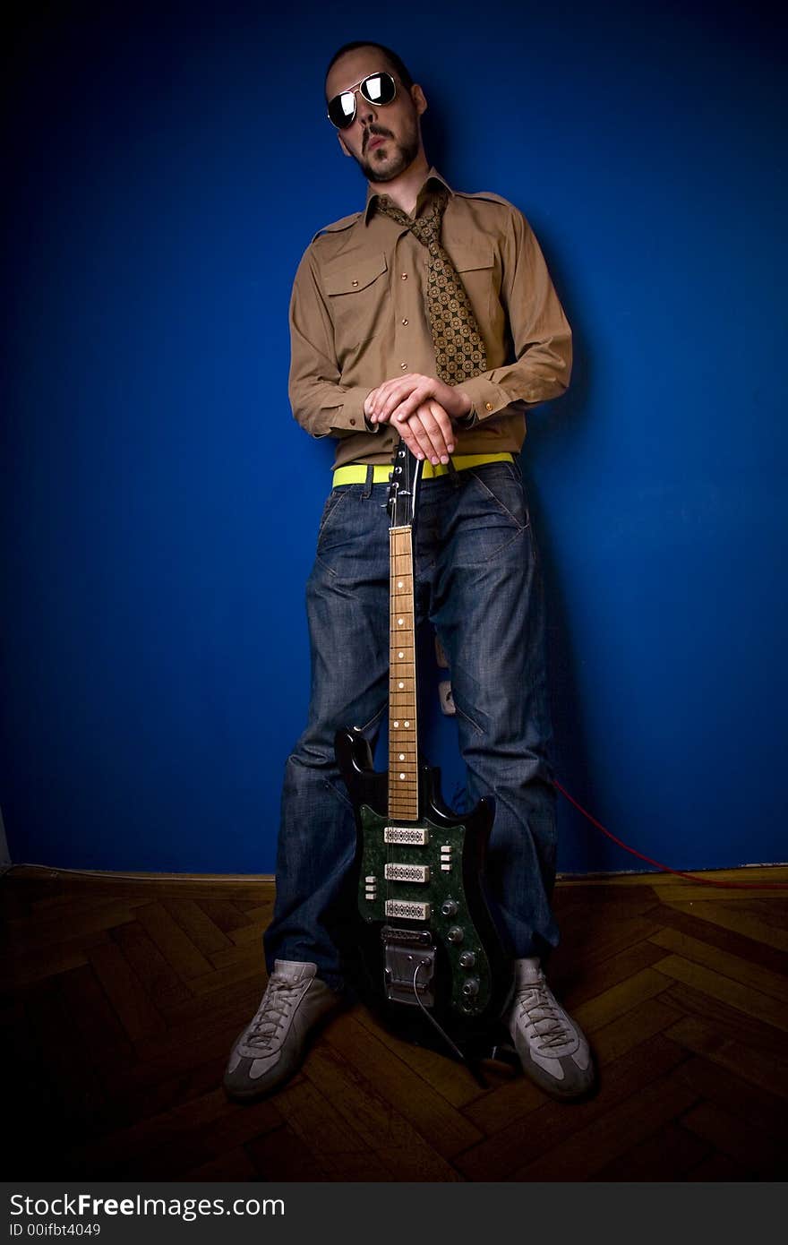 Guitar player in a cool pose, leaning against a blue wall. Guitar player in a cool pose, leaning against a blue wall.