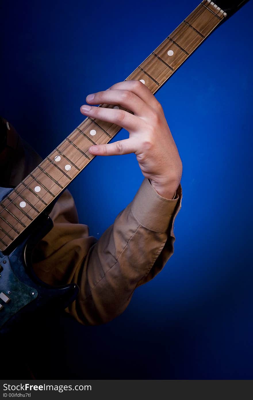 Guitarist hand on an electric guitar fretboard. Blue background. Guitarist hand on an electric guitar fretboard. Blue background
