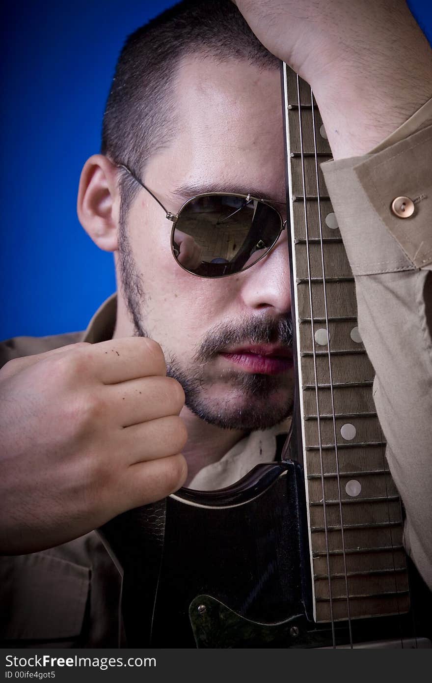 Guitar player with sunglasses in studio, leaning his head against the fretboard of his guitar, facing the camera. Guitar player with sunglasses in studio, leaning his head against the fretboard of his guitar, facing the camera.