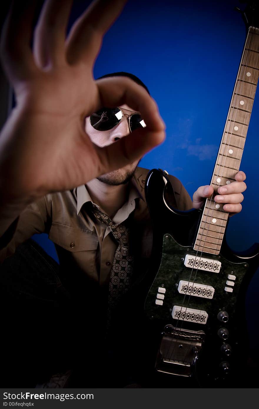 Guitar player with sunglasses in studio, giving an OK sign. Focus on guitarist. Guitar player with sunglasses in studio, giving an OK sign. Focus on guitarist.