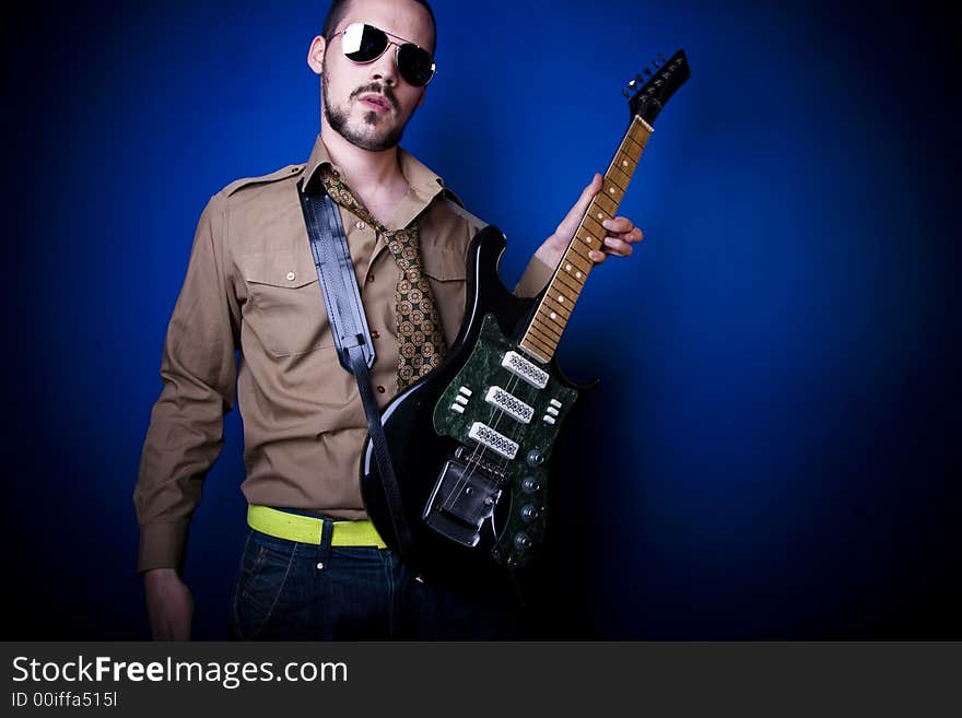 Guitar player with sunglasses in studio against a blue wall.