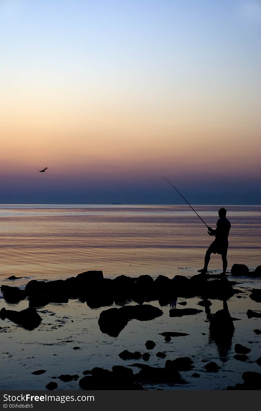 The young fisherman fishing on coast of the Atlantic ocean at a sunrise